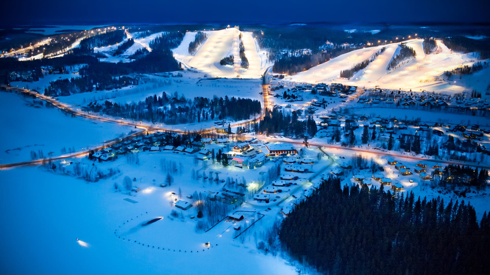 Himoksen valaistut rinteet talvi-illan ilmakuvassa
